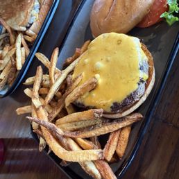 Build your own - A cheeseburger with melted cheese on a beef patty is placed on a black tray, alongside a sandwich with a bun and a side salad with lettuce and tomato. French fries are spread around the burger, and the tray is on a wooden table. The image captures a casual dining presentation with typical American fast-food items.