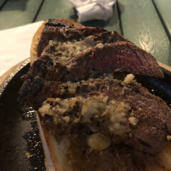 Caffrey's Tavern Backyard - Garlic steak sandwich- yumm but could shake the garlic smell for two days - The image features a garlic steak sandwich served on a black skillet, with two slices of toasted bread topped with cooked steak, melted cheese, and garlic. The sandwich is placed on a green wooden table, with a white napkin and a condiment container visible in the background. The focus is on the sandwich, highlighting the texture of the steak and the melted cheese. - American Near Me - Forked River, New Jersey