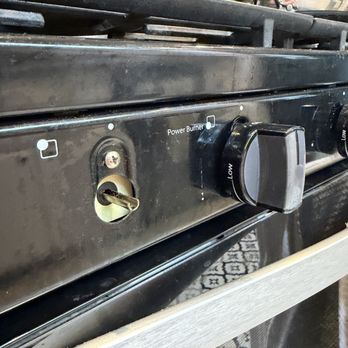 Kleen - The image shows a black stove with a key inserted into the ignition slot, located on the front panel. To the right of the key, there is a control knob labeled 'Power Burner' with settings from low to high. The stove appears to be in a kitchen or utility area, with some kitchen items visible in the background, including a pot on the stove and a bottle on the countertop. - Home Cleaning Near Me - Pasadena, California