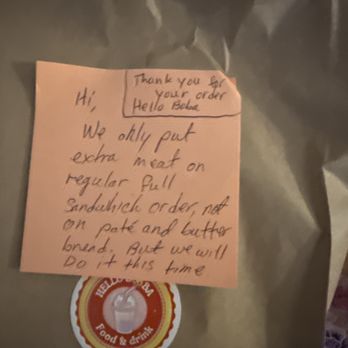 Hello Boba - A pink sticky note with handwritten text is affixed to a brown paper bag. The note explains that extra meat was added to a sandwich order, not on a pate and butter bread, and mentions a future order. The note is written in casual handwriting and is part of a food order, likely from a restaurant or takeout service. - Bubble Tea Near Me - Lowell, Massachusetts