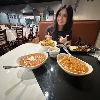 Taj Indian Cuisine - a woman sitting at a table with bowls of food - Indian Near Me - Fredericksburg, Virginia Taj Indian Cuisine - a woman sitting at a table with bowls of food - Indian Near Me - Fredericksburg, Virginia