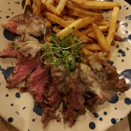 Beef Tenderloin - A dish featuring sliced beef tenderloin topped with melted cheese, served with French fries and garnished with microgreens.