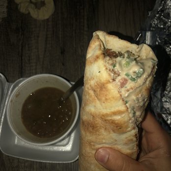 Cedars Restaurant - Habibi Falafel Wrap ma lentil soup - A person holds a large wrap filled with a creamy mixture, with a cup of soup on a foam tray nearby, on a wooden table. - Lebanese Near Me - Camp Hill, Pennsylvania