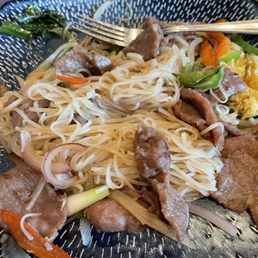 Stir fry beef pho - A dish of stir fry beef pho featuring rice noodles, sliced beef, vegetables, and scrambled eggs on a black patterned plate.