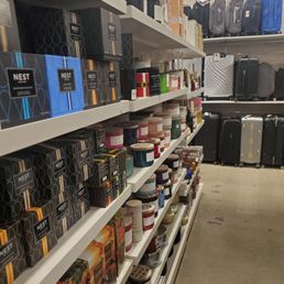 Retail store shelves display candles, gift boxes, and travel suitcases in various sizes and colors.