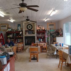 Panacea RV Park - Cozy café interior with dining tables, ceiling fans, decorative shelves, fireplace centerpiece, and customers enjoying breakf...