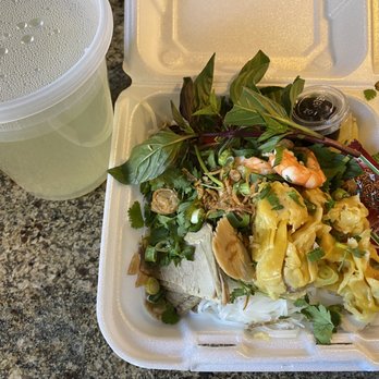 Basil Leaf Vietnamese Restaurant - Chicken broth with rice noodles, chicken , shrimp, pork, and wontons - A foam takeout box contains Vietnamese dishes with herbs, vegetables, and seafood, accompanied by a plastic cup of light-colored beverage on a granite surface. - Vietnamese Near Me - Albuquerque, New Mexico