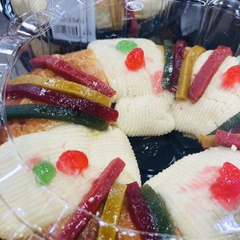 El Super - a variety of cakes in plastic containers - A cake with fruit toppings, including red and green candied cherries, is displayed in a clear plastic container, with a visible price tag. - Grocery Near Me - Tuscon, Arizona