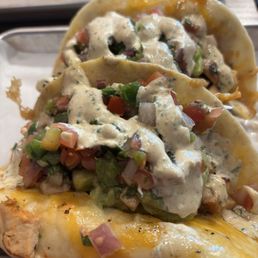 Chicken chipotle tacos - Two tacos with chicken, diced vegetables, and a creamy sauce are served on a tray, garnished with chopped greens and tomatoes.