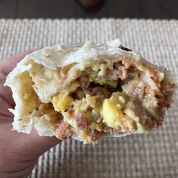Bacon Burrito - A person holds a breakfast burrito filled with eggs, meat, and potatoes, with the bite revealing the ingredients inside.