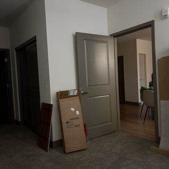 Lets Fix It - A room with an open door leading to another area, cardboard boxes, and a wooden panel leaning against the wall, indicating moving or renovation. - Handyman Near Me