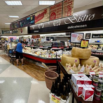 Ralphs - Cheese section in a grocery store with large cheese wheels, cheese products, and a customer shopping. - Grocery Near Me - Temecula, California