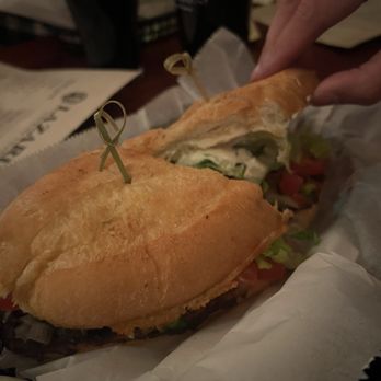 Lazarus Brewing - Torta De Carnitas - A sandwich with fresh baguette bread, lettuce, tomato, and other fillings is being held by a person at Lazarus Brewing, with dark drinks in the background. - Breweries Near Me - Austin, Texas