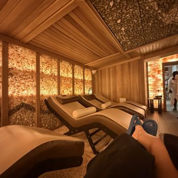 World Spa - A person is seated on a massage chair in a spa room with wooden walls and ceiling, illuminated by warm lighting, with a textured ceiling panel. - Day Spas Near Me - Brooklyn, New York
