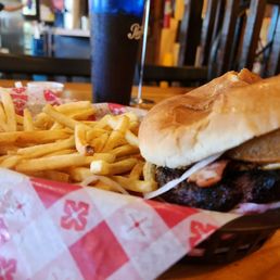 Western Burger - A burger with a beef patty, bacon, and cheese in a bun, accompanied by French fries in a basket, on a wooden table.