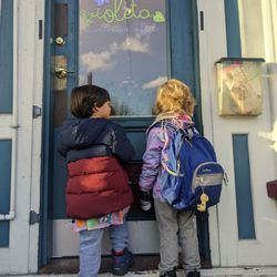 Violeta Montessori School - Two young children in winter coats looking through the window of Violeta Montessori School.