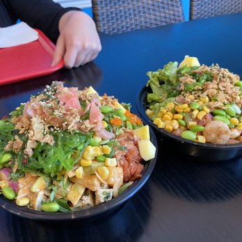 Poke Land Extra - Two poke bowls with vegetables, corn, edamame, and toppings are placed on a black table in a restaurant setting. - Poke Near Me - Redding, California