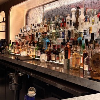 Ginger's - A bar area featuring a marble countertop and a backlit display of various liquor bottles, including spirits and liqueurs. - Cocktail Bars Near Me - Dallas, Texas