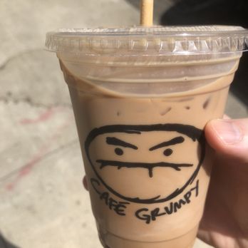 Café Grumpy - All price and no size makes Jack a grumpy boy. - A cold coffee beverage in a clear plastic cup with a lid, featuring a hand-drawn face and the text 'Café Grumpy'. - Coffee & Tea Near Me - Brooklyn, New York