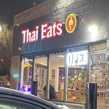 Thai Eats - Thai Eats, a Thai restaurant, features a black exterior with illuminated signs including a neon 'OPEN' sign and a bright logo. The interior is visible through large glass windows. - Noodles Near Me - Oak Lawn, Illinois