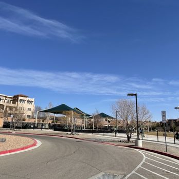 A Park Above - To the back of the park. - A parking lot with shade canopies, trees, and nearby buildings, under a clear blue sky with some clouds. - Parks Near Me - Rio Rancho, New Mexico