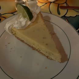 Home-made Key Lime Pie - A slice of key lime pie with a graham cracker crust, topped with whipped cream and a lime wedge, served on a white plate.