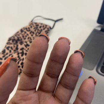 Pro's Nails By Vy - The image shows a hand with painted nails, featuring a leopard print design, held up in front of a white surface. Behind the hand, a leopard print face mask is placed on the surface, and part of a laptop is visible on the right side of the image. The setting appears to be an indoor workspace or desk area. - Nail Salons Near Me - Mesa, Arizona
