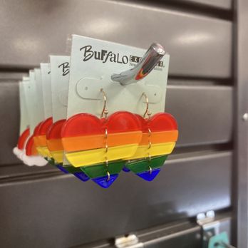 Buffalo Exchange - Love 'em - Rainbow-colored heart-shaped earrings made of translucent plastic are attached to a display card with the store's branding. The earrings are arranged in a row, hanging from a metal hook, and are set against a metallic background, likely part of a retail display for accessories. - Women's Clothing Near Me - Austin, Texas