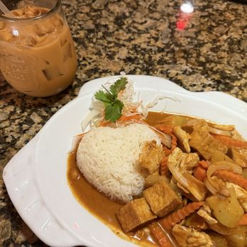 Ploy Thai - Massaman curry with heart shape rice! - A Thai curry dish featuring rice, mixed vegetables, and tofu served on a white plate, with a garnish of cilantro and shredded vegetables. A glass of iced Thai tea with milk and ice cubes is placed nearby on a speckled granite countertop. The setting appears to be in a restaurant or home dining area. - Thai Near Me - Brandon, Florida