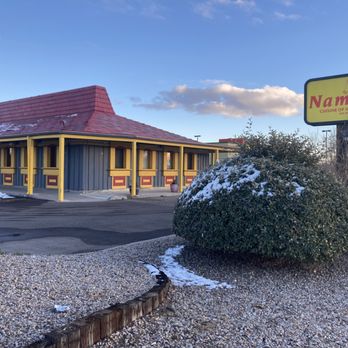 Namaste - Namaste.  Exterior.  You can see it used to be a Pizza Hut. - The image depicts the exterior of Namaste, an Indian and Nepalese restaurant, with a building that has a red, sloped roof and yellow trim around the windows and support beams. A large bush with snow on it is in the foreground, alongside a sign displaying the restaurant's name and cuisine type. The ground has patches of snow, and the sky is partly cloudy with blue and white clouds. The setting appears to be during winter, with a parking lot visible around the building. - Indian Near Me - Rio Rancho, New Mexico