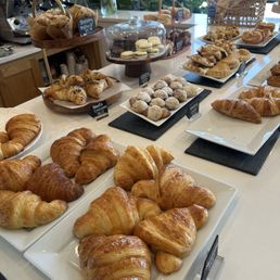 Baked goods section - Assorted baked goods such as croissants, cookies, and pastries are arranged on white plates and black slate trays in a bakery or cafe setting.