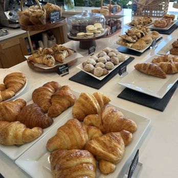 Panicafé - Baked goods section - Assorted baked goods such as croissants, cookies, and pastries are arranged on white plates and black slate trays in a bakery or cafe setting. - Bakeries Near Me - Spring, Texas