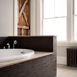 Kevin Edge Photography - Modern bathroom with a freestanding tub, large window for natural light, and dark tiling. Combines luxury and functionality.