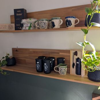 Jennings Java Coffee Roasters - Two wooden shelves hold coffee mugs, a coffee grinder, and potted plants, with a wall and countertop in the background. - Coffee Roasteries Near Me - Columbus, Ohio