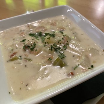 Boulder Social - Cup of clam chowder - A bowl of clam chowder with a creamy texture, garnished with chopped herbs, served in a white dish on a wooden table. - New American Near Me - Boulder, Colorado