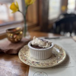 Chocolate Chile Cream Pot - Chocolate dessert in a ramekin with whipped cream topping, placed on a floral plate on a wooden table at Hell's Backbone Grill & Farm.