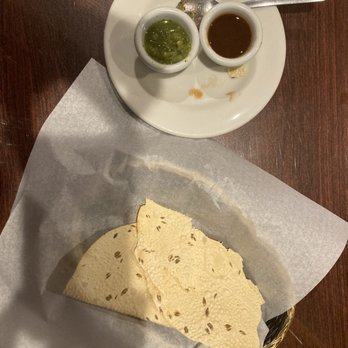 Namaste - Namaste.  Papadum. 2 Crispy crackers with lentil flour. - A white plate holds two small bowls of dipping sauces, one green and one brown, with a spoon resting on the plate. Below, a basket lined with parchment paper contains several pieces of papadum, a thin, crispy Indian flatbread, on a wooden table surface. - Indian Near Me - Rio Rancho, New Mexico