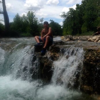 Happy Hollow Grocery - a man sitting on the edge of a waterfall - Grocery Near Me - Concan, Texas