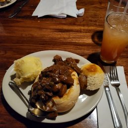 Irish beef stew with guinness and a cocktail. - A plate features Irish beef stew with mashed potatoes and a bread roll, served on a wooden table with a drink in a tall glass.