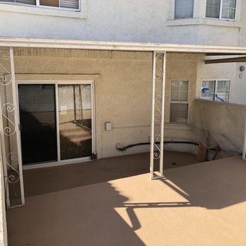 Pasadena Handyman - A small outdoor patio with a metal-framed roof and decorative supports, attached to a beige residential building with sliding glass doors. - Handyman Near Me