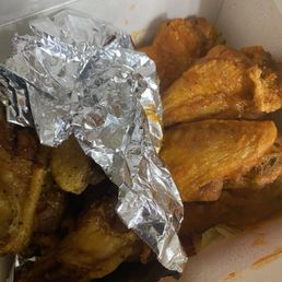 Atl Dry Rub - Chicken wings and drumsticks with a golden-brown coating are inside a takeout box, some covered with aluminum foil.