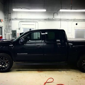 Leo's autoworks - Putting new wheels on - A black Chevrolet Silverado pickup truck is parked inside a garage with white walls, fluorescent lighting, and visible electrical wiring. - Auto Repair Near Me - Patchogue, New York