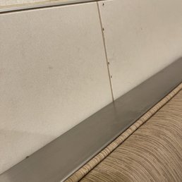 Ants in that corner booth - The image shows a tiled wall with a metal trim and a cushioned seat with striped fabric, possibly in a public space or restaurant.