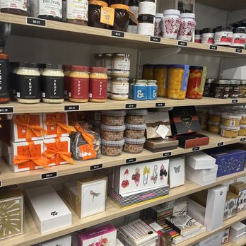 Belladukes - A gourmet purveyors dream - Shelves filled with various products including jars of jam, gift boxes with ribbons, and decorative items such as butterfly and floral designs. The products are arranged in an organized manner, with price tags visible. The store appears to sell gourmet food items, gifts, and decorative products, with multiple shelves holding different categories of items. - Coffee & Tea Near Me - Boca Raton, Florida