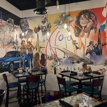 Circa69 - Mural in Circa69 bar - A mural on a restaurant or cafe wall depicts diverse artistic images, including a woman with glasses, a fighter jet, a classic car, and various figures, with hanging light bulbs overhead. - Cocktail Bars Near Me - Jensen Beach, Florida