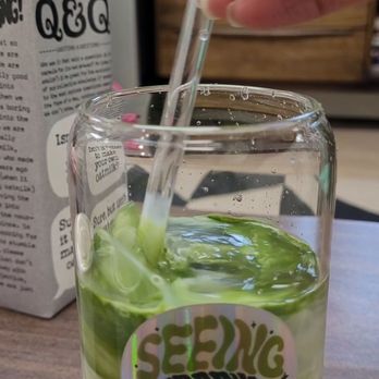 Seeing Green Studio - My handcrafted matcha latte - A handcrafted matcha latte with lime slices is in a glass with a straw, placed on a wooden table at Seeing Green Studio. - Paint-Your-Own Pottery Near Me - Halethorpe, Maryland