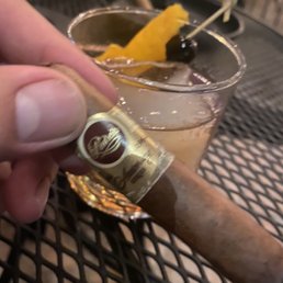 a hand holding a cigar and a glass of alcohol