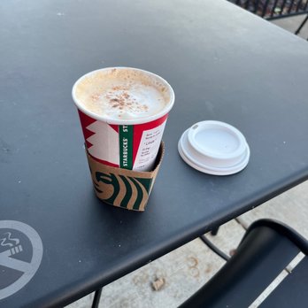 Starbucks - Small! - A Starbucks coffee cup with a cardboard sleeve and a white plastic lid placed on a black outdoor table. - Coffee & Tea Near Me - Brookfield, Wisconsin