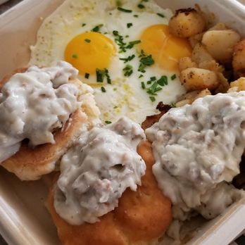 First Watch - A breakfast plate featuring biscuits topped with turkey sausage gravy, two fried eggs, and roasted potatoes, served in a takeout container. - Breakfast & Brunch Near Me - Newtown Square, Pennsylvania