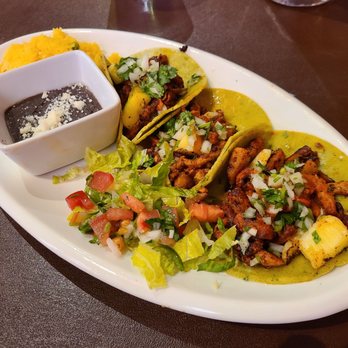 Fiesta Oaxaca - Al Pastor tacos... pork, Pineapple... was good! Did not need salsa or anything, the flavor alone was great! - A white oval plate holds three tacos with seasoned meat, topped with onions and cilantro, accompanied by a side salad and black bean sauce. - Mexican Near Me - Santa Fe, New Mexico
